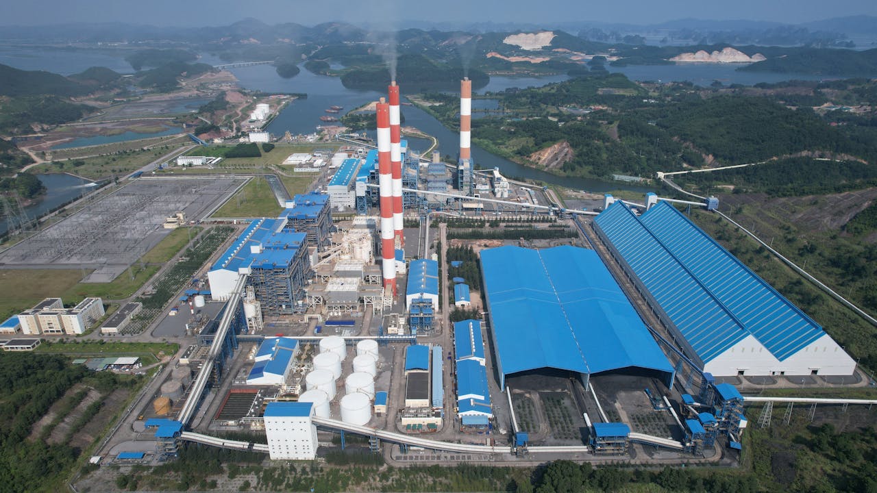 Aerial view of a major industrial plant in Cẩm Phả, Quảng Ninh, Vietnam, with chimneys and blue-roofed structures.